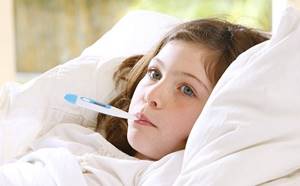 Больная девочка лежит в постели с градусником во рту
