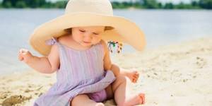 Девочка в шляпе сидит на песке