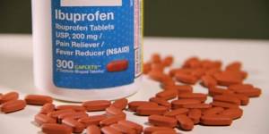 Ибупрофен в банке и рассыпанные таблетки на белом столе
