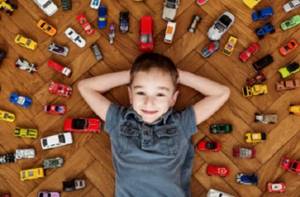 Мальчик лежит на полу, вокруг него множество машинок
