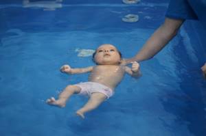 Малыша держат на воде на спинке ножками вперёд