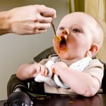 Ребенка кормят морковным пюре с ложки