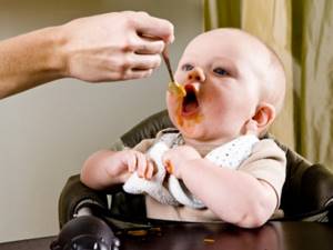 Ребенка кормят морковным пюре с ложки