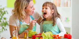 Женщина кормит ребенка овощами