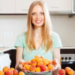 Женщина с абрикосами сидит на кухне